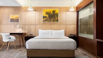 Quarto de hotel moderno com uma cama grande, uma escrivaninha, uma cadeira e duas pinturas nas paredes.