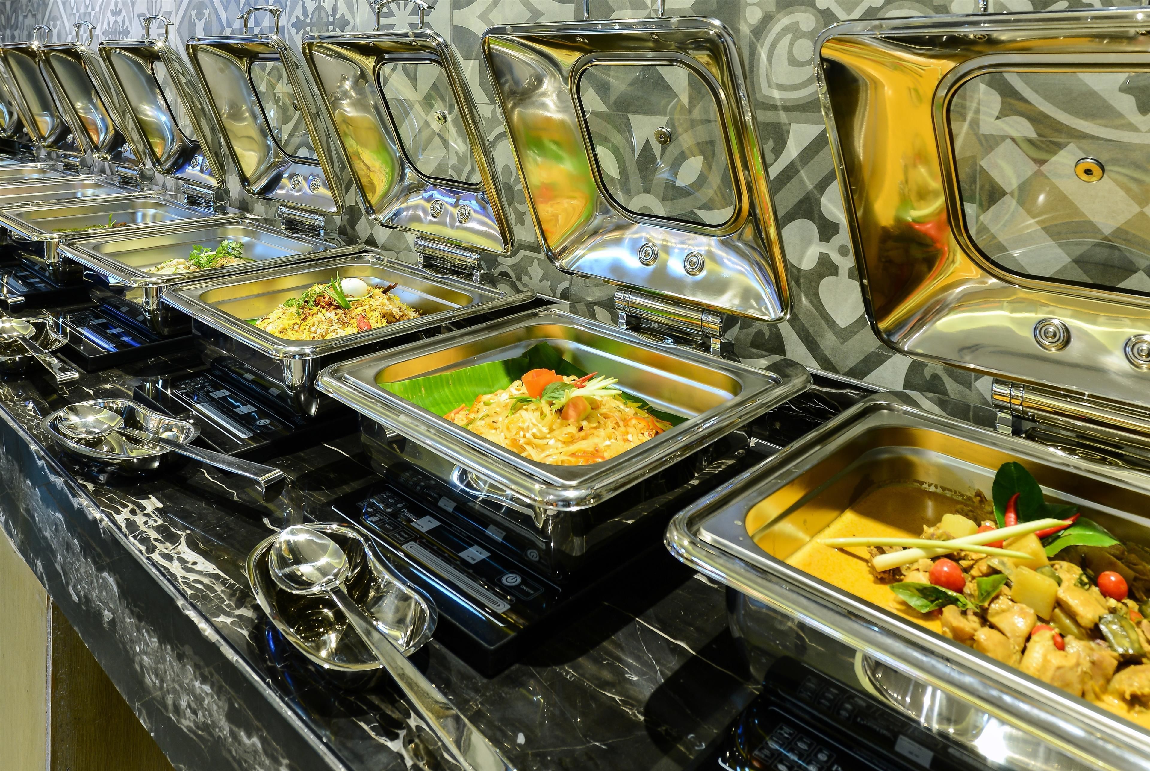 Un buffet con diversi piatti in contenitori metallici, disposti su un bancone in marmo nero.