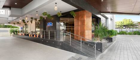 A modern hotel entrance with a spacious lobby, a staircase, and a sign indicating a restaurant.