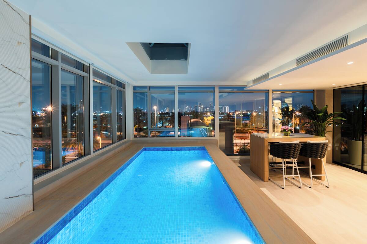 Una piscina interior moderna con vistas a la ciudad, zona de bar y amplios ventanales.