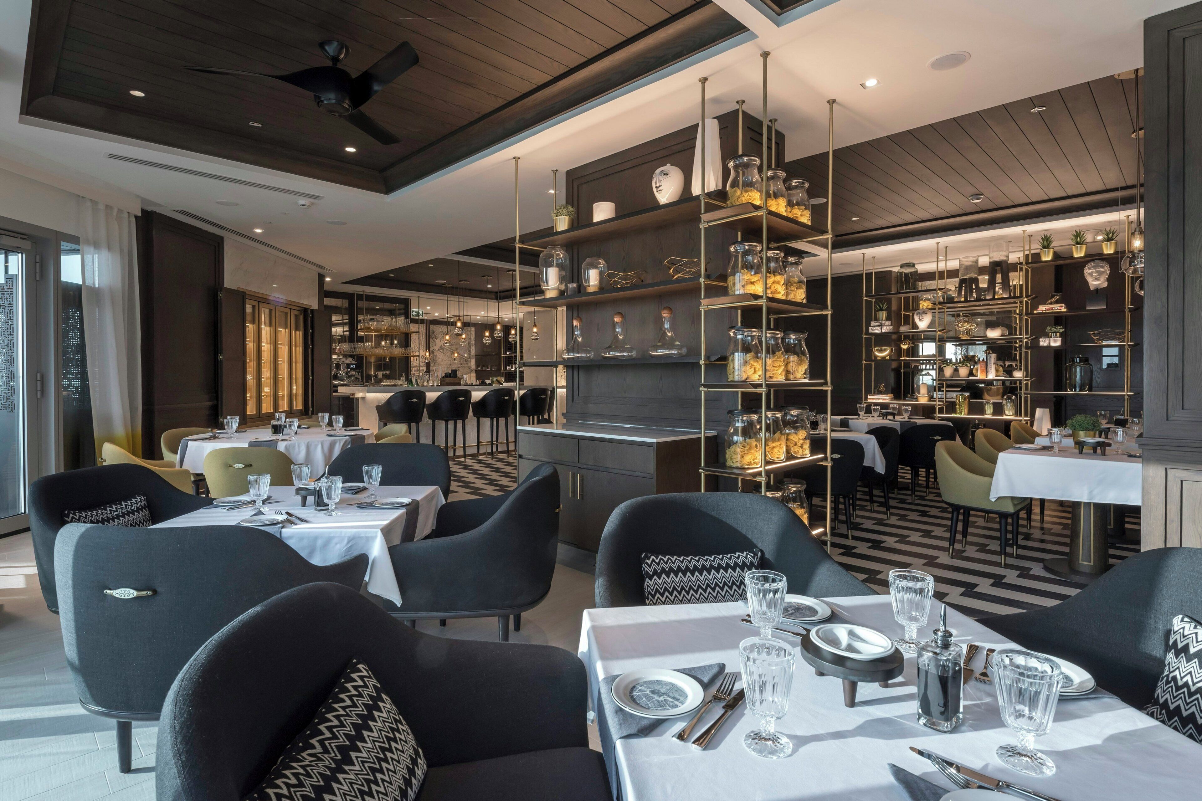 A restaurant with tables set for dining, a bar area, and shelves with decorative items.