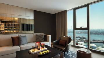A modern hotel room with a large window, a sofa, a coffee table with fruits and candles, and a view of the cityscape.