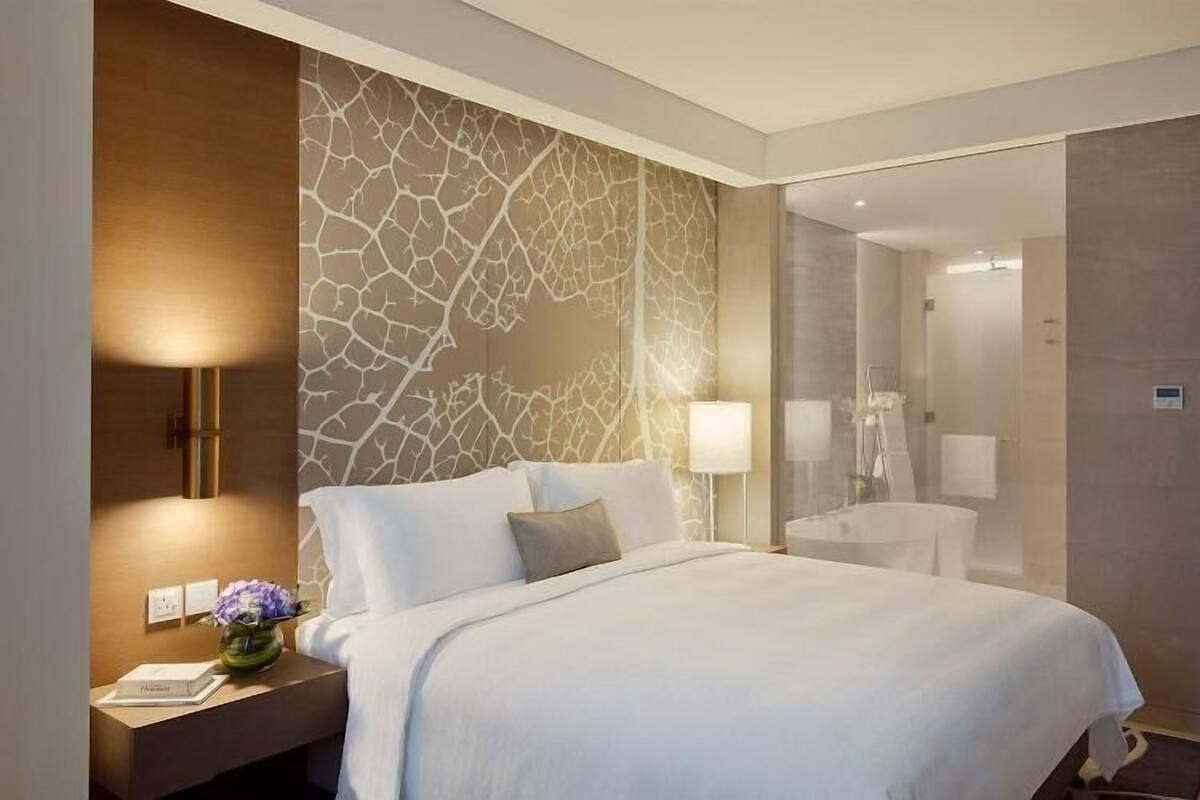 Habitación de hotel con cama, lámparas de noche, mesita de noche y baño visible a través de una puerta abierta.