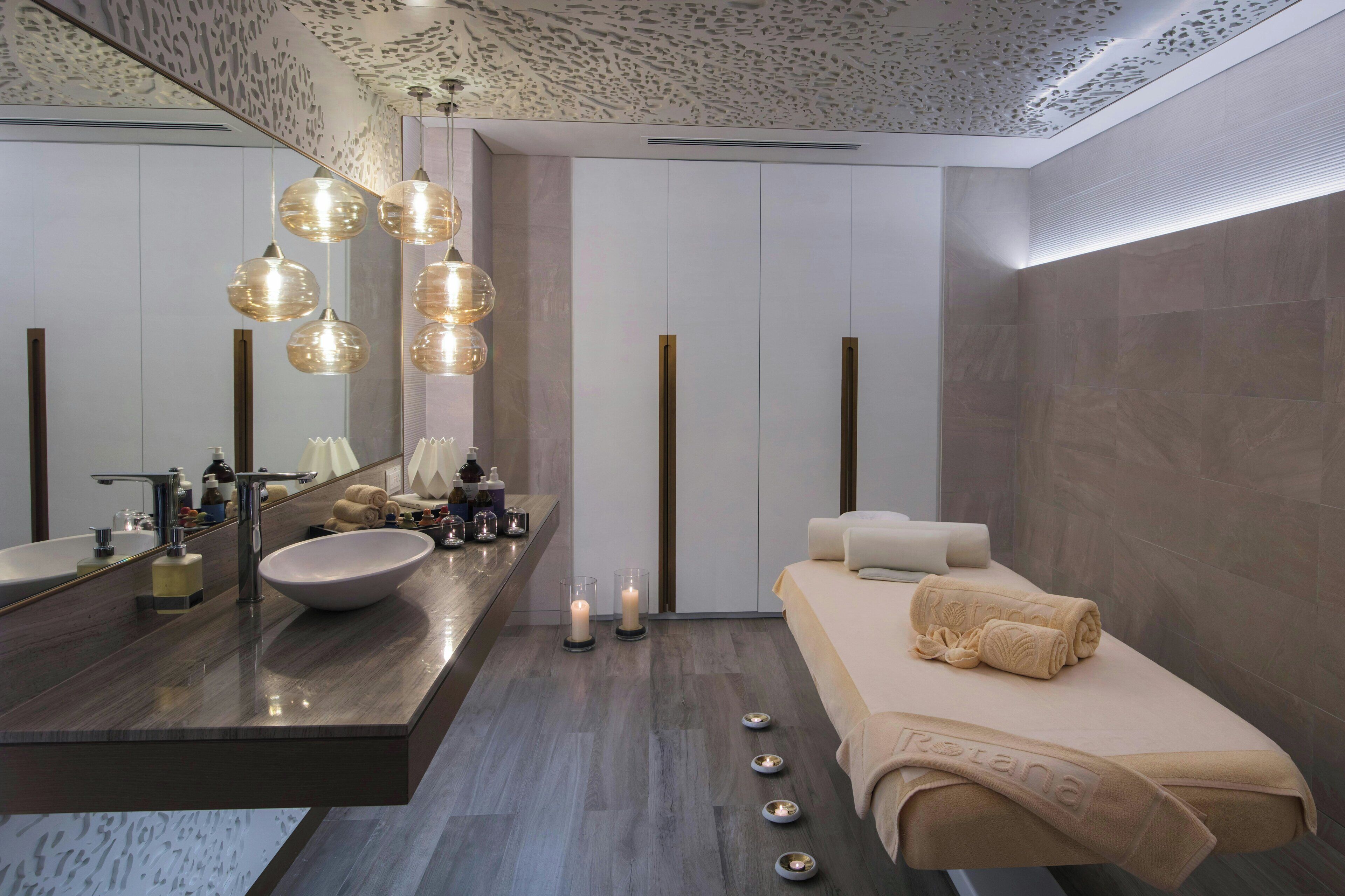 A modern bathroom with a large mirror, a round sink, and a bed with towels.