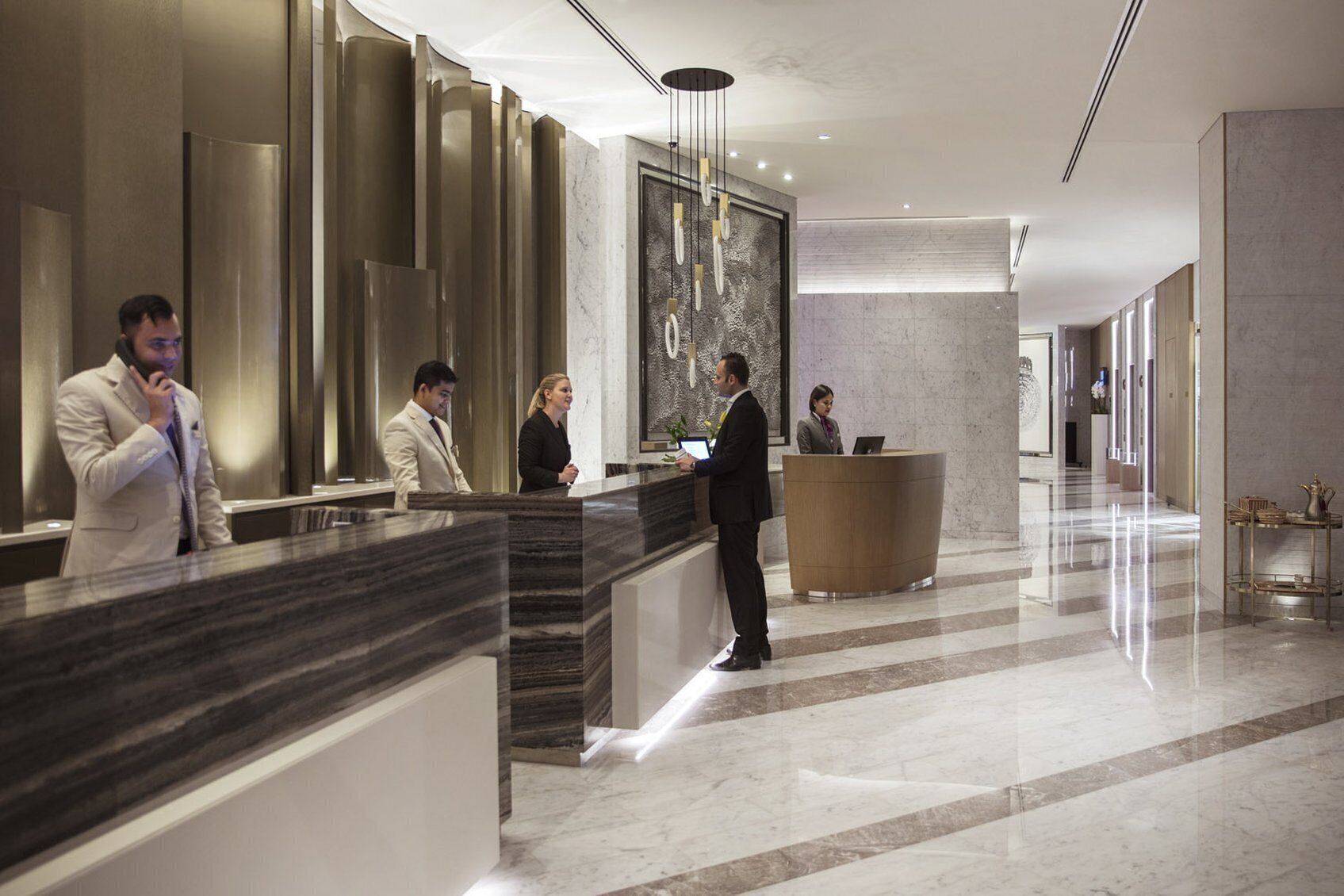 Uma área de recepção de hotel moderna, com piso de mármore, balcão de atendimento e uma grande pintura abstrata na parede.
