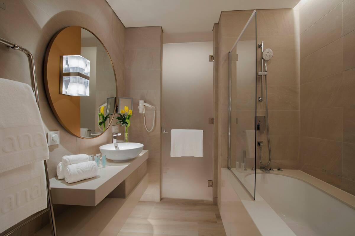 Un baño moderno con un espejo redondo, un lavabo, una bañera y una ducha.