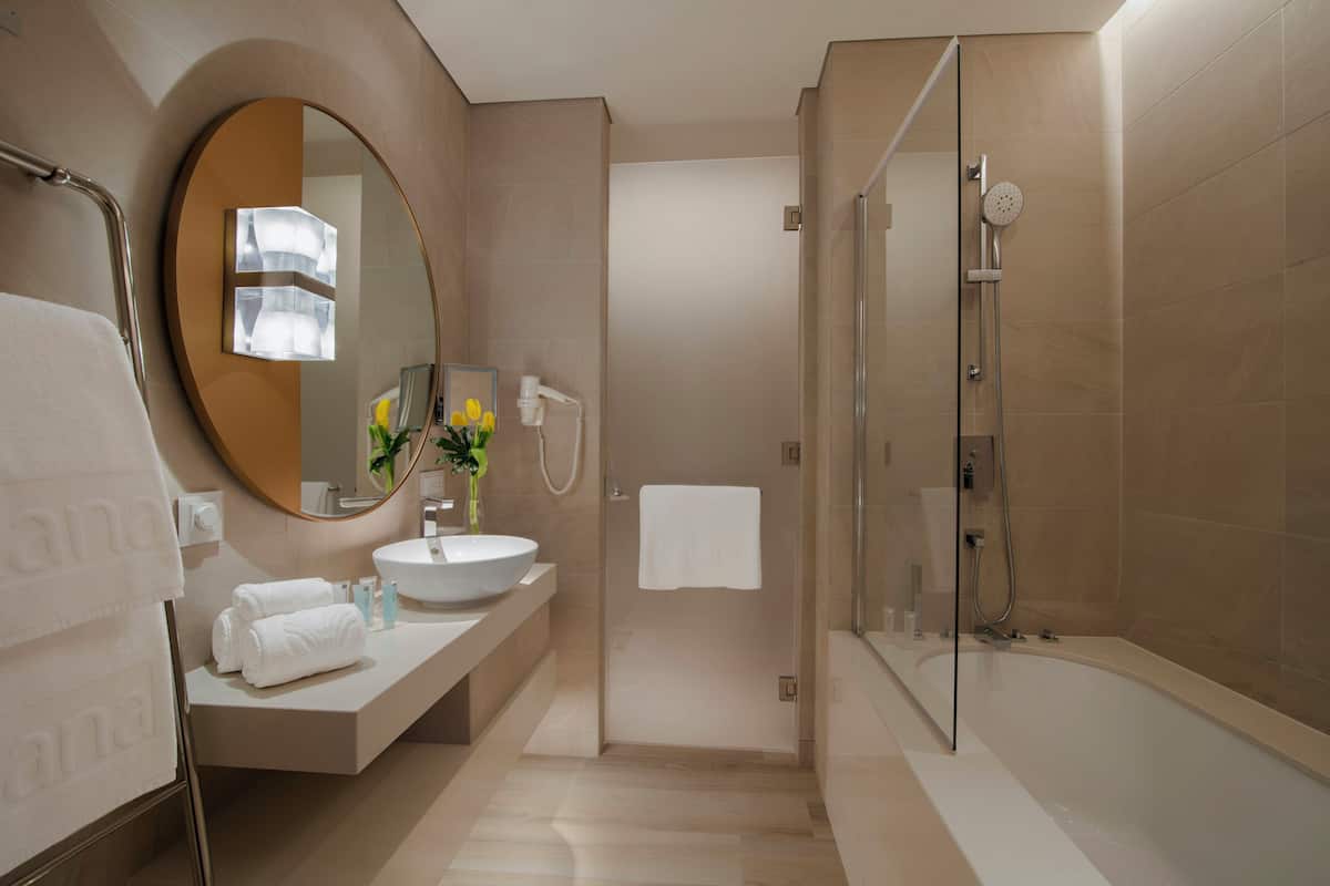 A modern bathroom with a round mirror, a sink, a bathtub, and a shower.