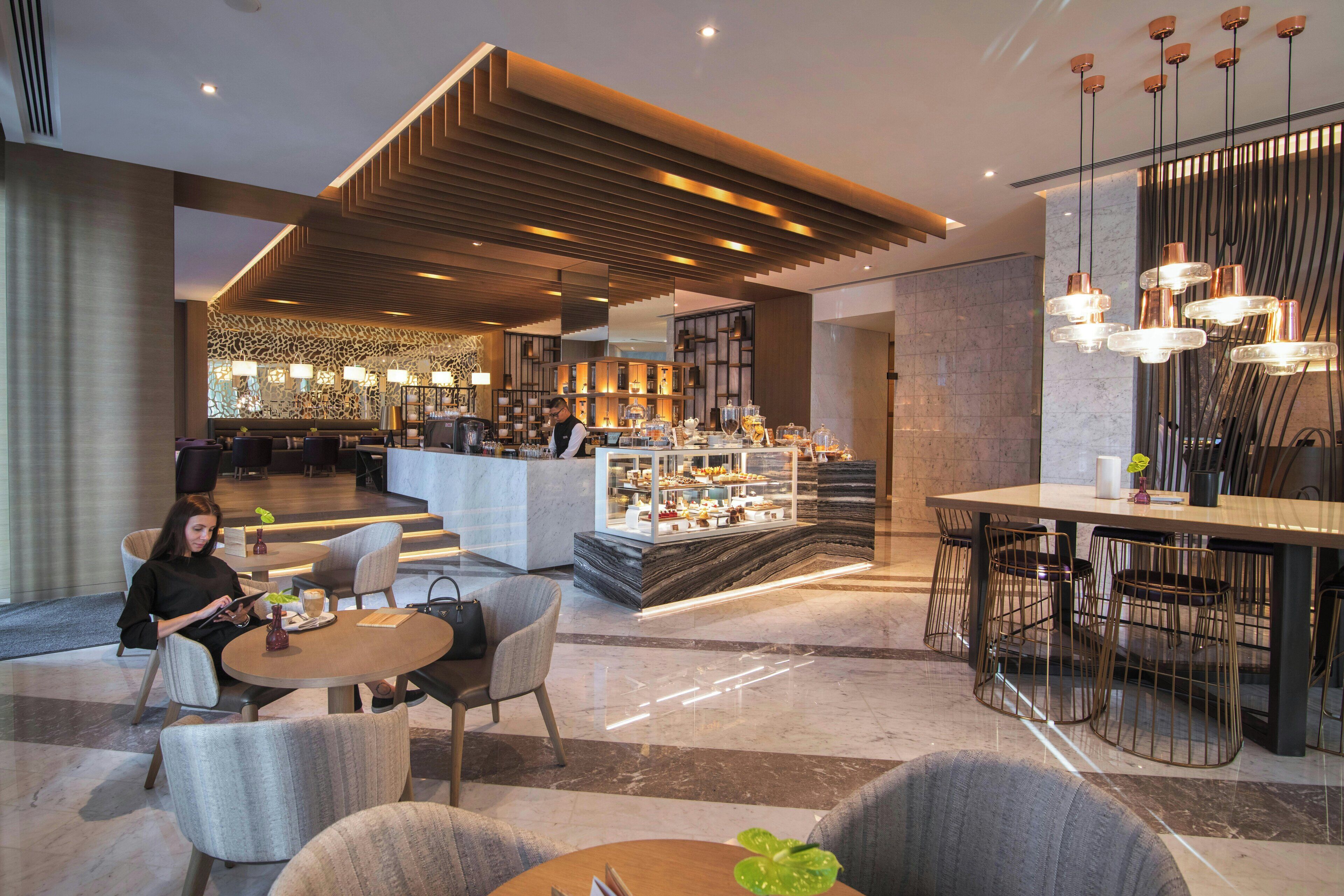 A modern hotel lobby with a bar area, seating arrangements, and a decorative ceiling.