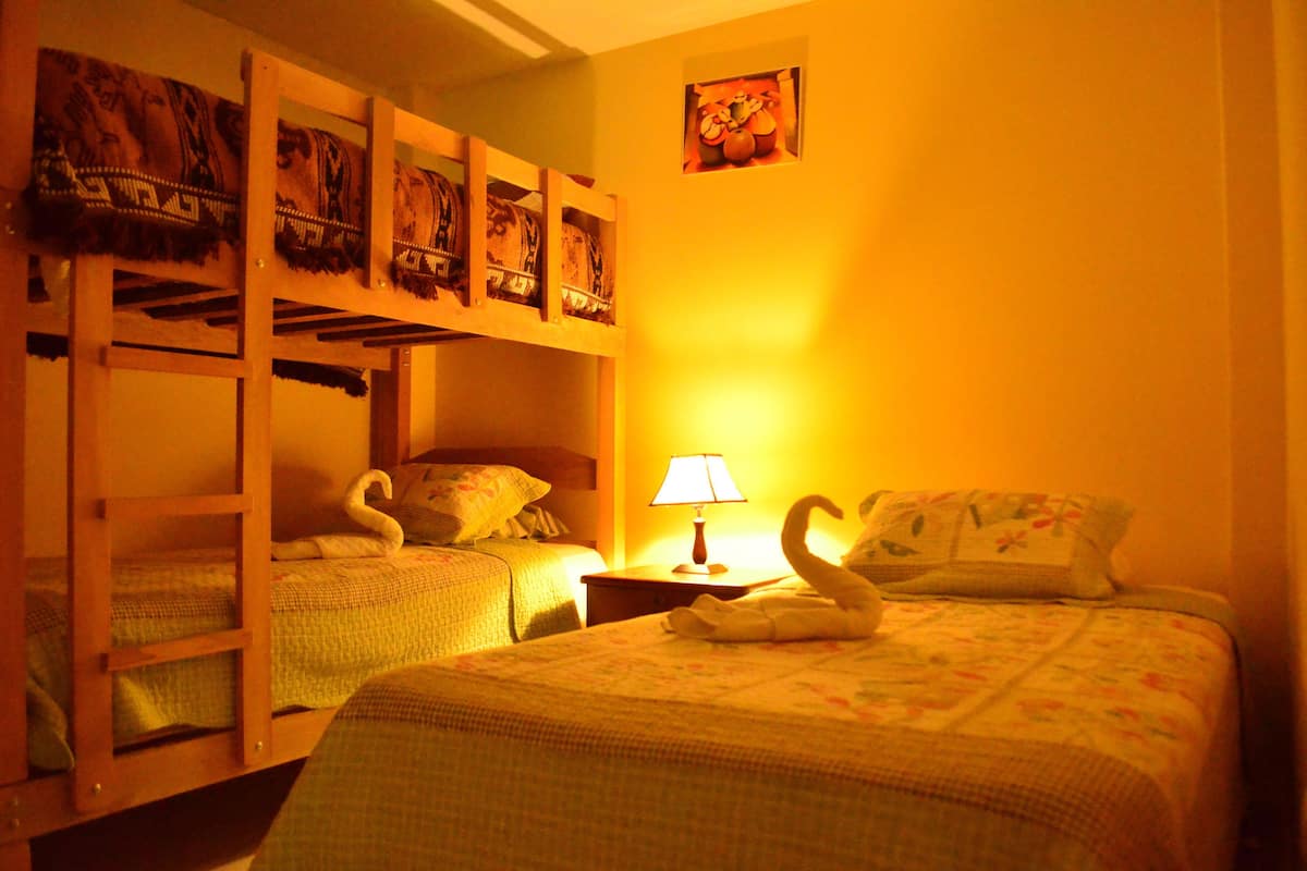 Ein Zimmer mit Etagenbetten, einem Einzelbett, einem Nachttisch mit Lampe und einem Wandbild.