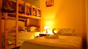Una habitación con literas, una cama individual, una mesita de noche con lámpara y un cuadro colgado en la pared.