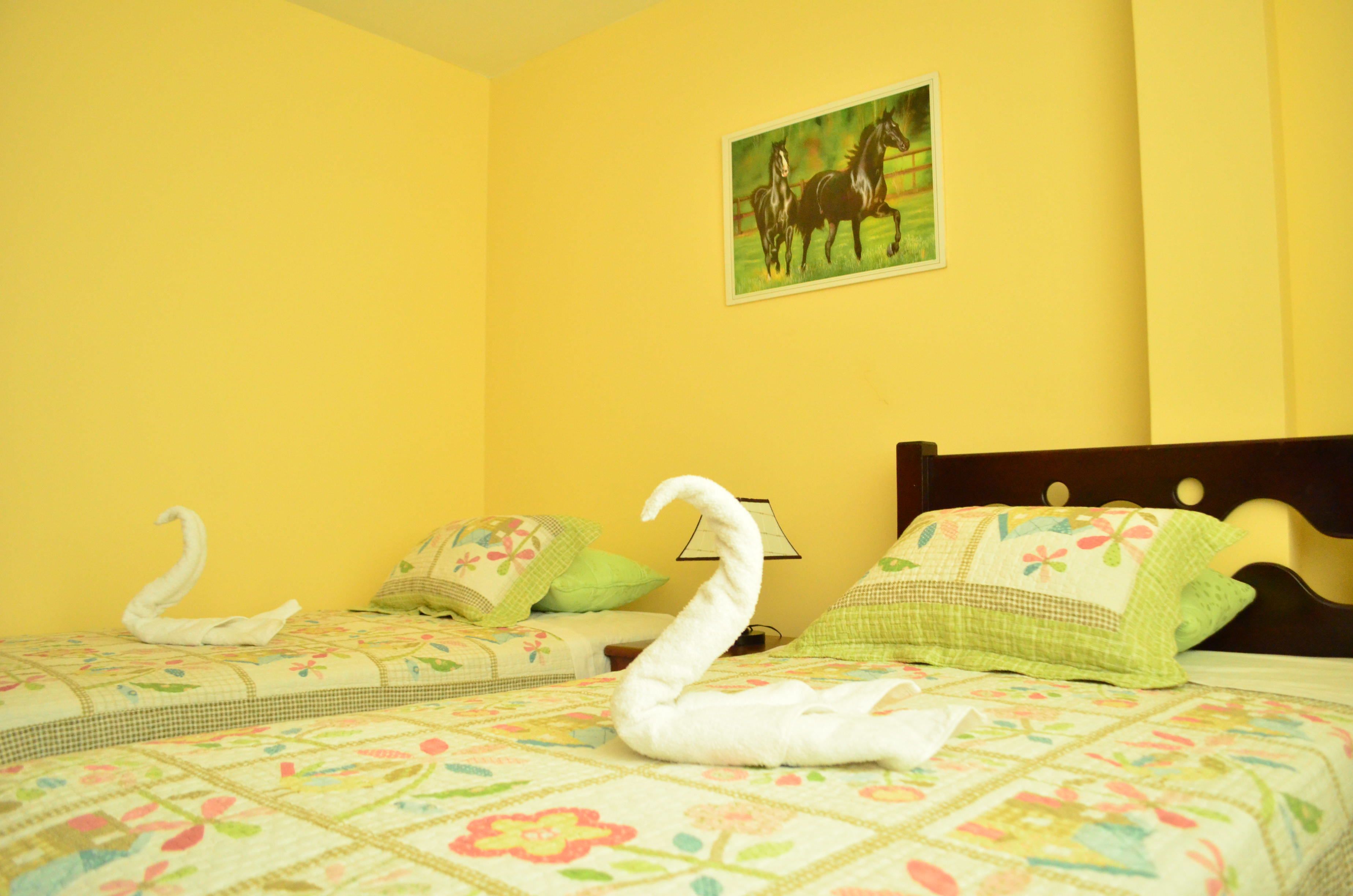 Habitación de hotel con dos camas, ropa de cama estampada con motivos florales, un cuadro de caballos y una almohada con forma de cisne.