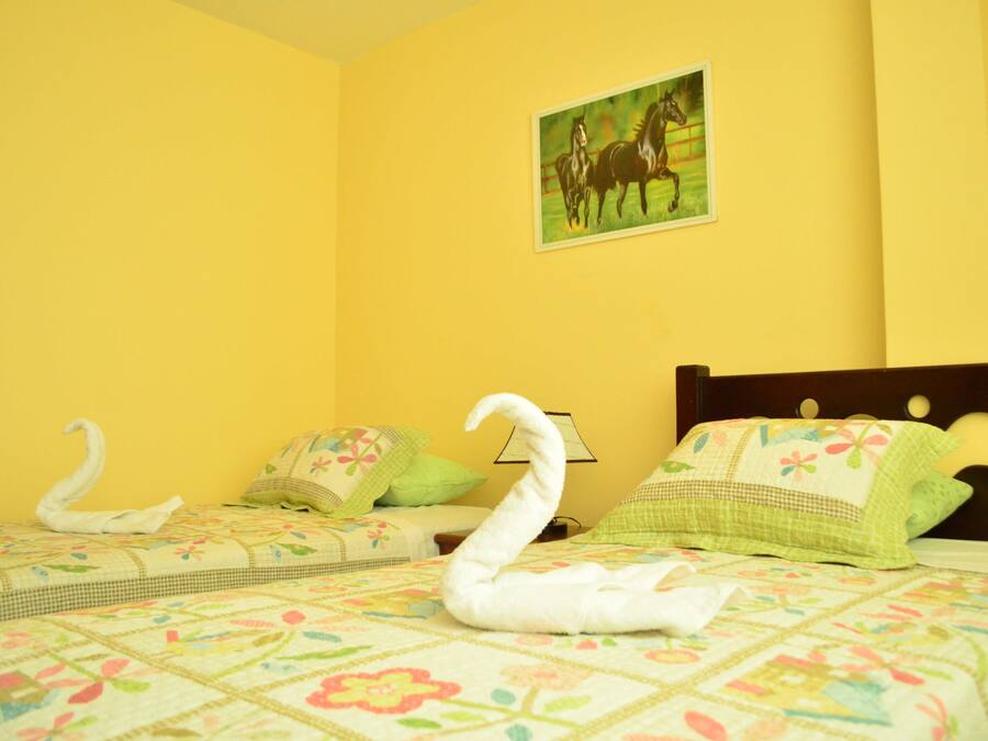 Habitación de hotel con dos camas, ropa de cama estampada con motivos florales, un cuadro de caballos y una almohada con forma de cisne.
