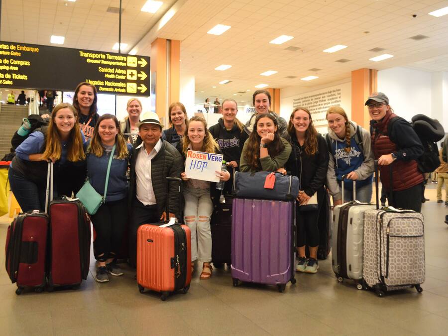 A group of people with luggage in an airport setting, featuring signs for 'Puertas de Embarque' and 'Transporte Terrestre'.