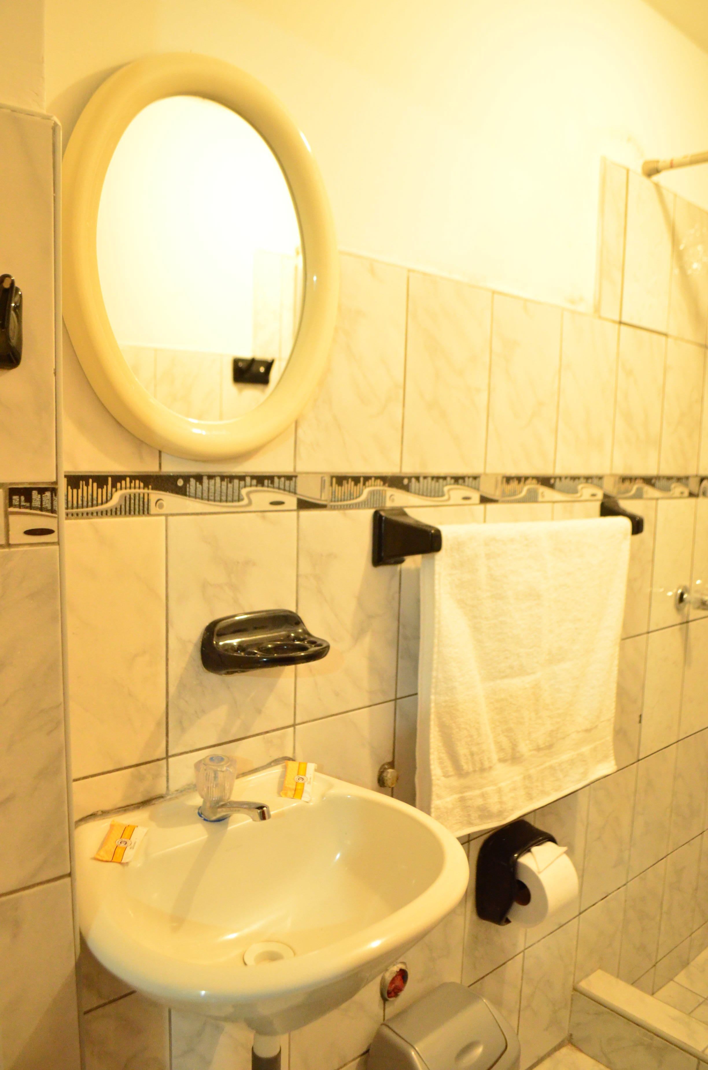 Baño con lavamanos, espejo, toallero, dispensador de papel higiénico y secador de manos.