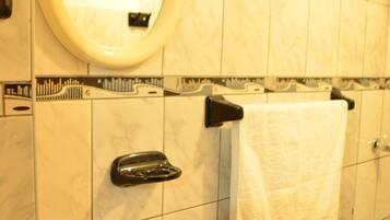 Baño con lavamanos, espejo, toallero, dispensador de papel higiénico y secador de manos.