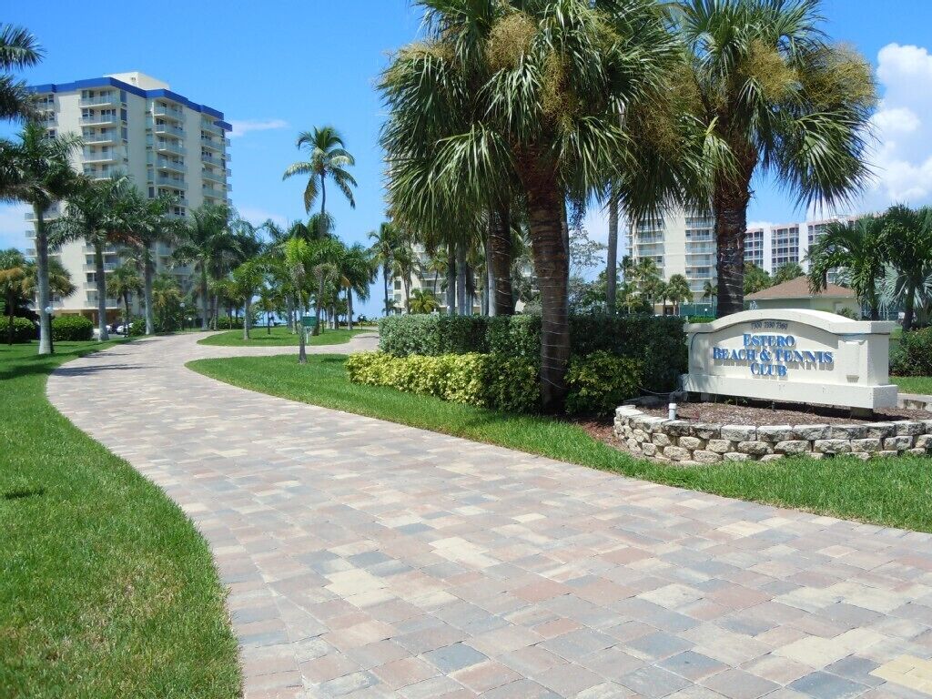 A paved pathway leading to a sign for the Estero Beach & Tennis Club.