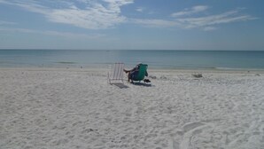 En strand med en person, der sidder i en stribet strandstol.