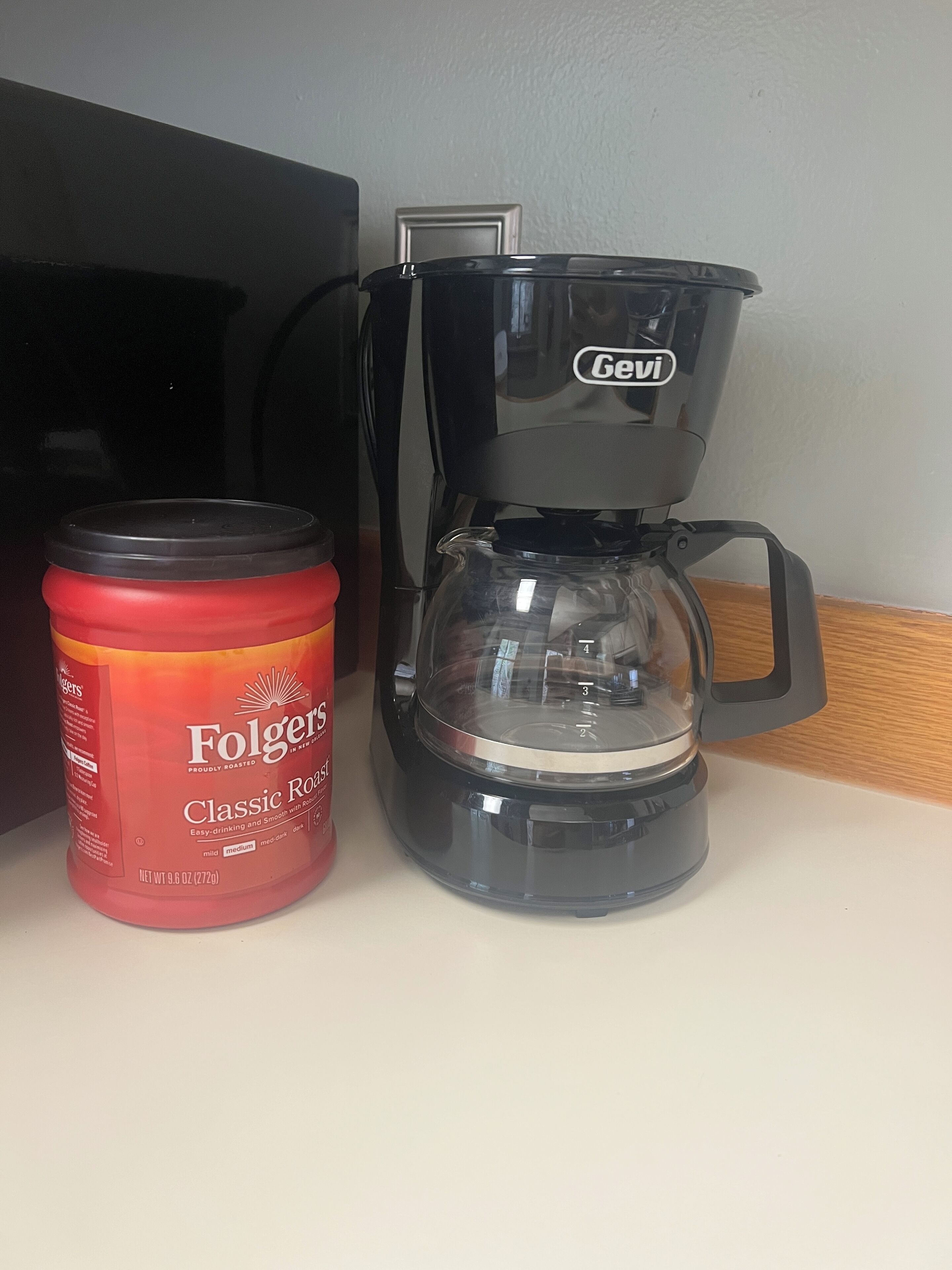 A coffee maker and a container of Folgers Classic Roast coffee on a countertop.