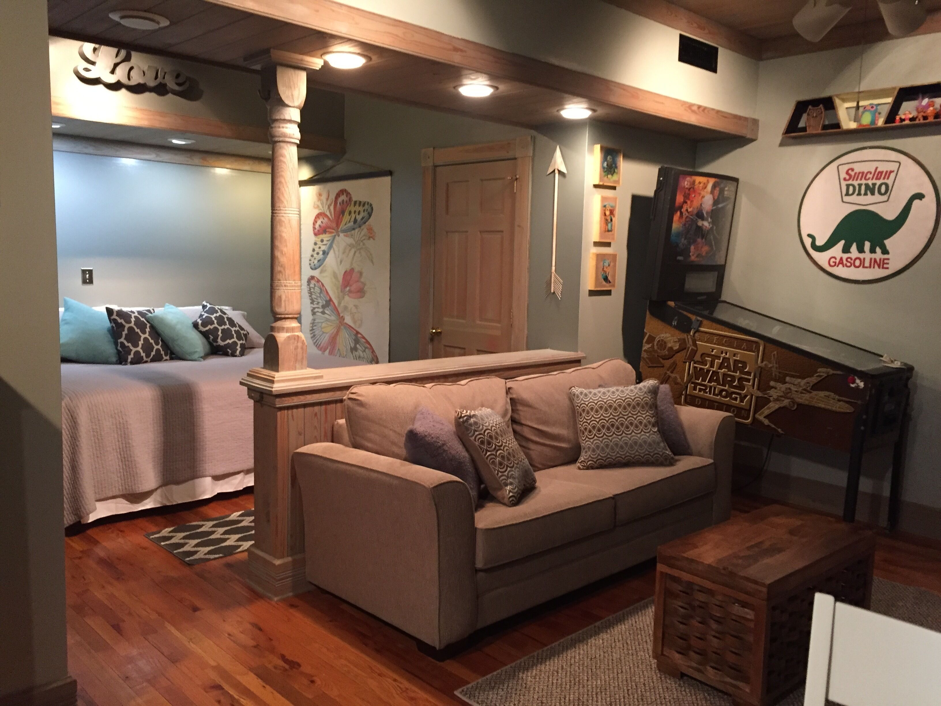 A cozy living room with a sofa, a coffee table, and a TV. There is a bed with a headboard and a wall with a dinosaur logo.