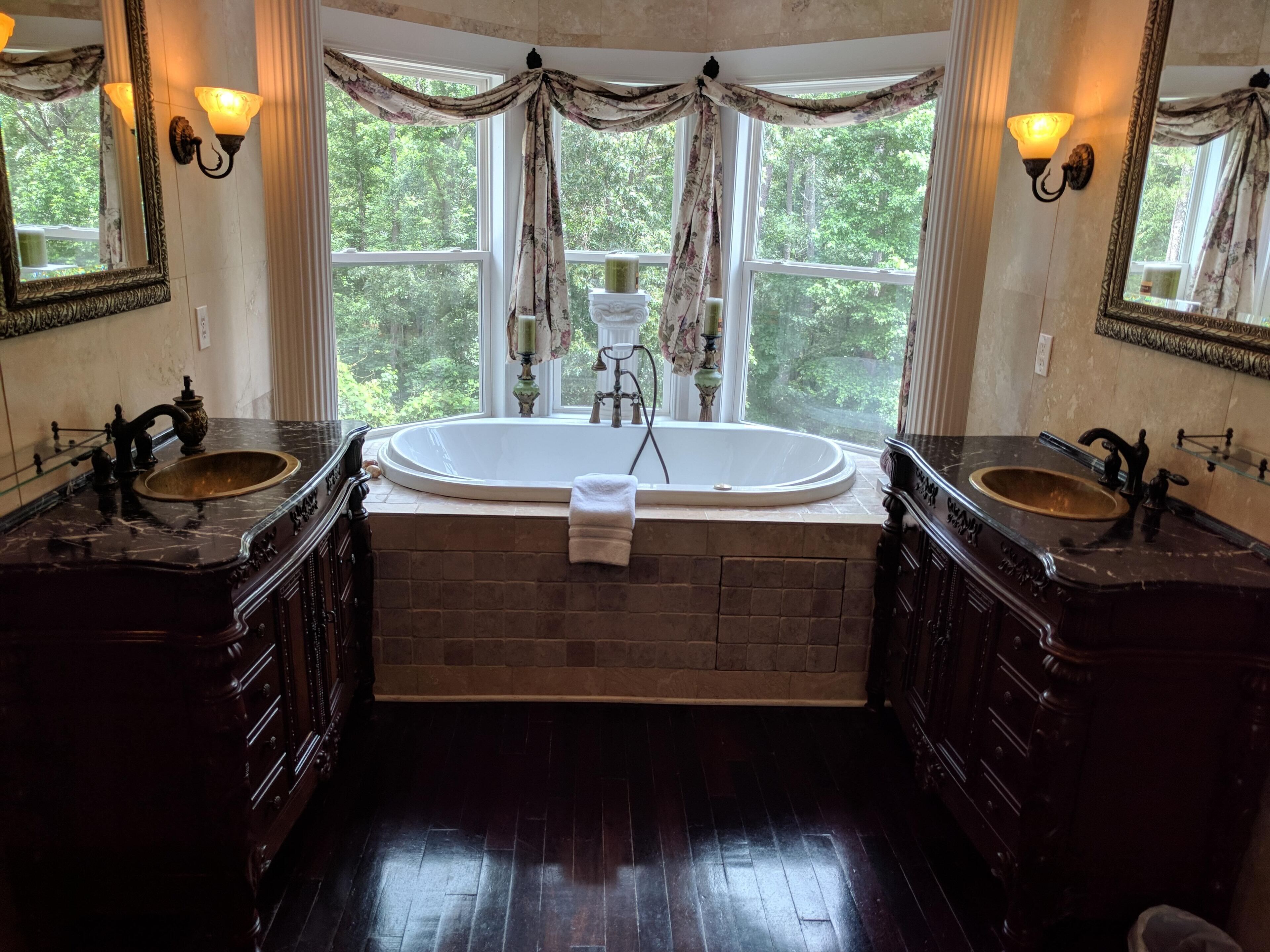 A bathroom with two sinks, a large bathtub, and a window with curtains.