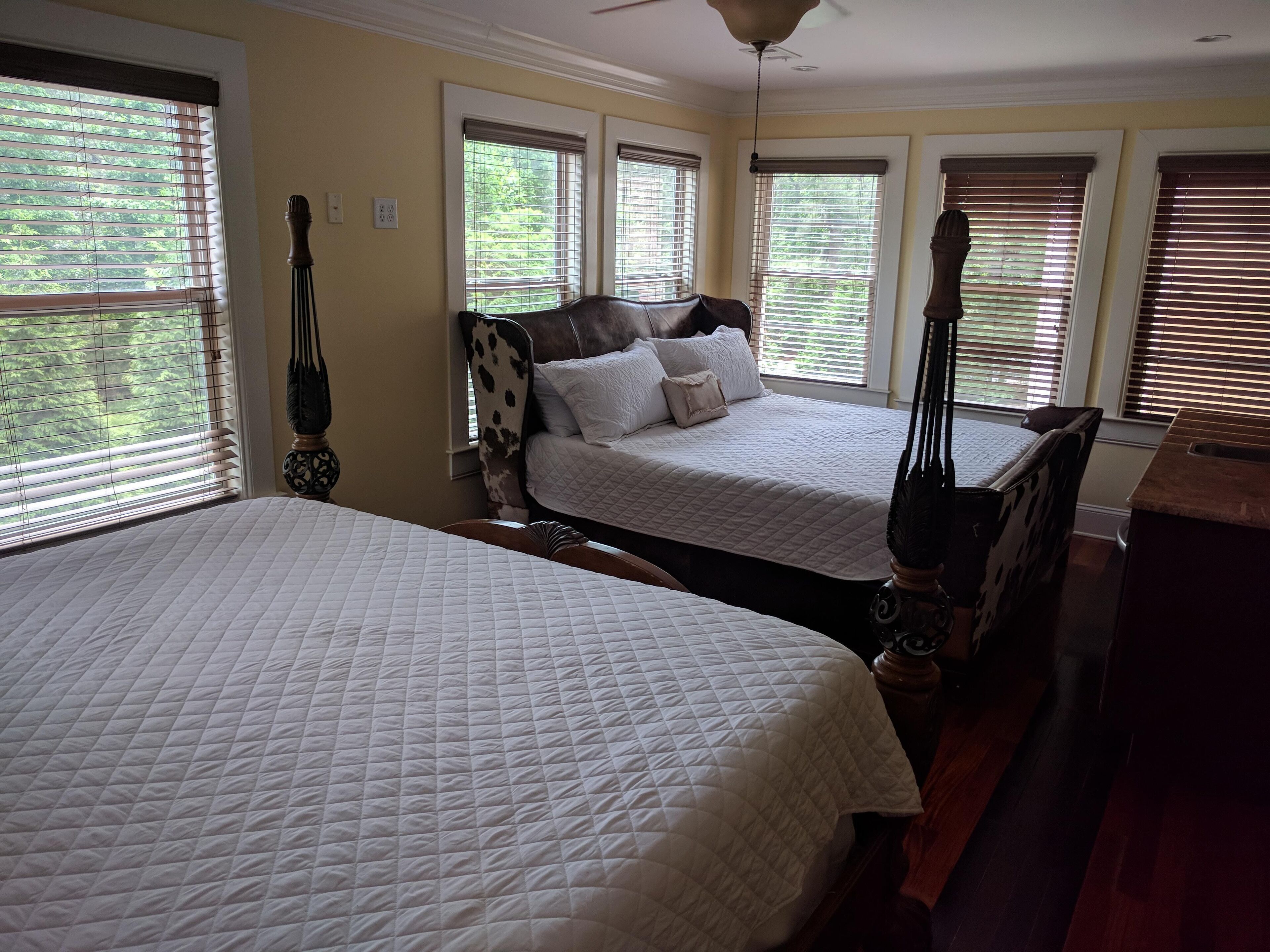 A bedroom with two beds, large windows, and a ceiling fan.