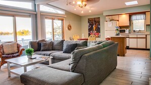 A modern living room with a sectional sofa, a small coffee table, and a wicker chair. There is a kitchen area with a microwave and a sink. - Colonial Beach Bay house with views & canoe (Westmoreland County)