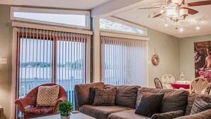 A living room with a large window, a ceiling fan, and a dining area with a table and chairs. - Colonial Beach Bay house with views & canoe (Westmoreland County)