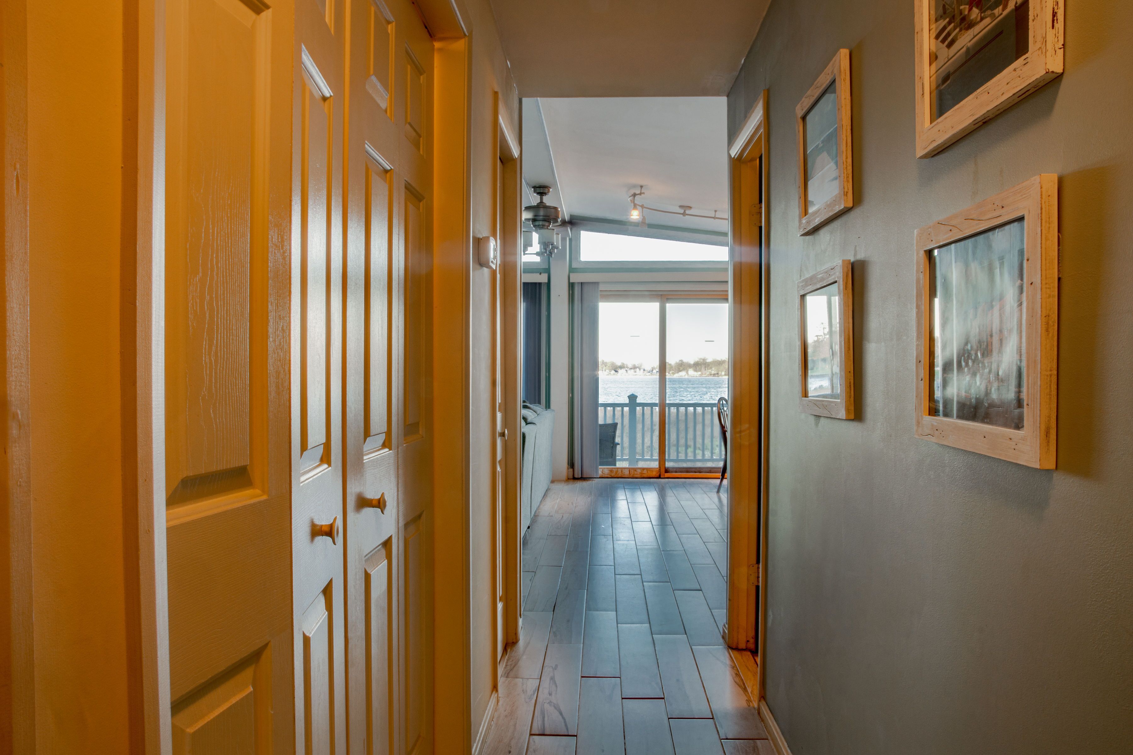 A hallway with wooden doors, a view to a balcony, and framed pictures on the wall.
