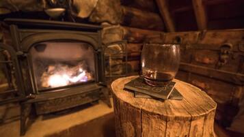 A glass of wine on a wooden coaster next to a stone fireplace with a visible fire.
