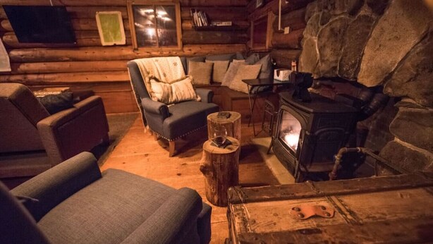 Ein gemütliches Blockhaus-Interieur mit Kamin aus Stein, einem blauen Sessel und einem Holztisch.