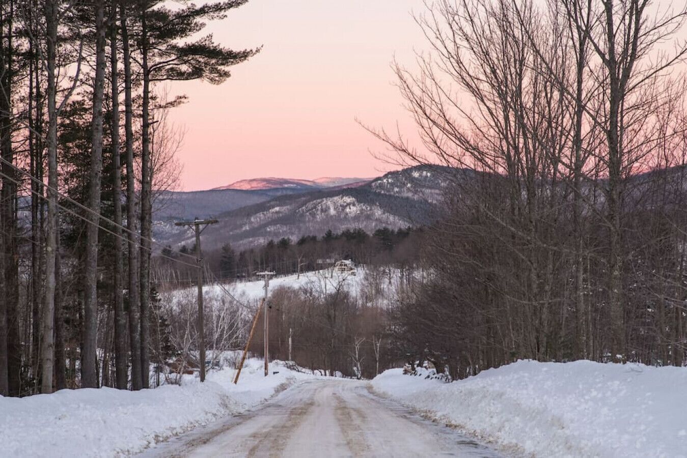 Une route enneigée, bordée d’arbres, avec des montagnes en arrière-plan.