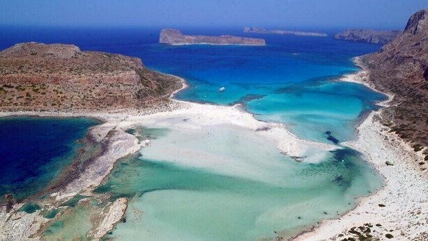 Vista aérea de una zona costera con aguas azul turquesa, playas de arena y terreno rocoso.