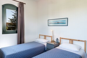 Ein Schlafzimmer mit zwei Betten, einem Nachttisch, einer Lampe, einem gerahmten Bild an der Wand und einem Fenster mit Vorhängen.
