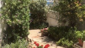 Um caminho no jardim com plantas em vasos e vista para o mar.