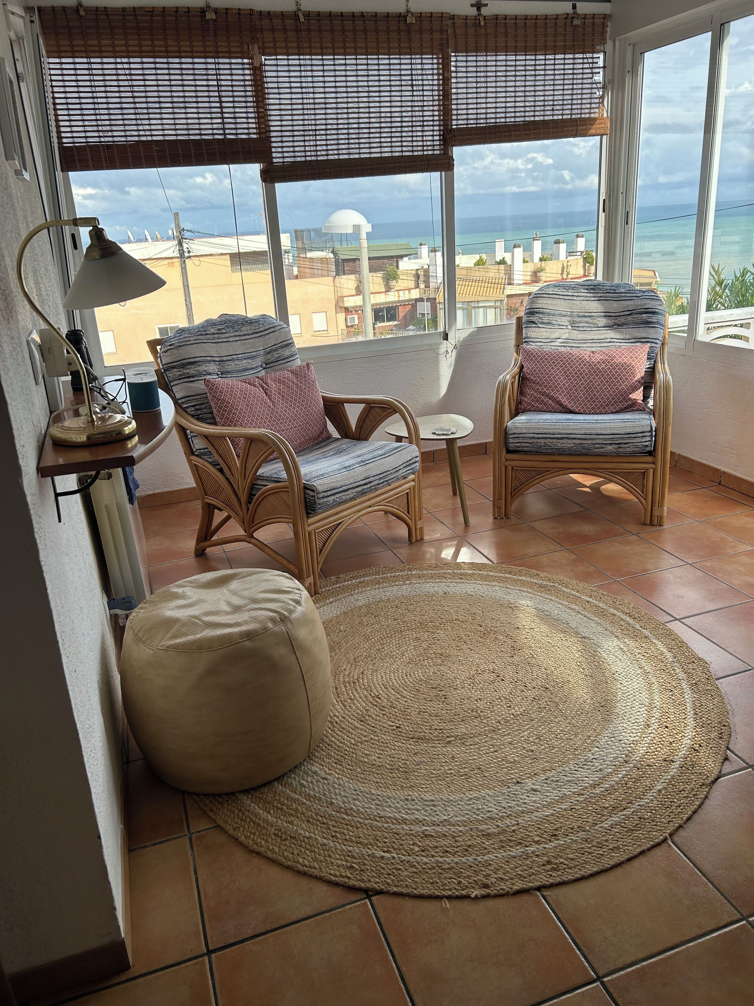 A room with two wicker chairs, a small table, a lamp, and a large woven rug.