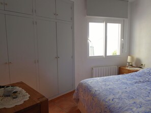 A bedroom with a bed, a wardrobe, a window, a bedside table, and a radiator.