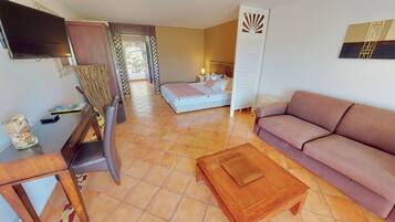 A hotel room with a bed, a sofa, a TV, a wooden table, and a decorative wall piece.