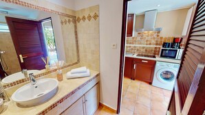 A bathroom with a sink, mirror, and towel rack. The adjacent room contains a kitchen with a microwave, stove, and washing machine. - modern studio sea view orient bay 50m from the beach (cul de sac)