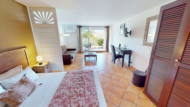 A hotel room with a bed, a desk, a chair, a small table, and a view of the outdoors. - modern studio sea view orient bay 50m from the beach (cul de sac)
