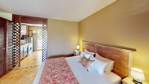 A hotel room with a bed, nightstand, and a view of the kitchen and dining area through an open door. - modern studio sea view orient bay 50m from the beach (cul de sac)