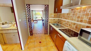 A compact kitchen with a sink, stove, and microwave. A dining area is visible through a doorway. - modern studio sea view orient bay 50m from the beach (cul de sac)