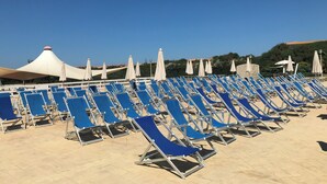 Una playa con filas de sillas azules y sombrillas blancas.