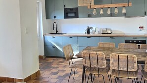 Een moderne keuken met lichtblauwe kastjes, een houten eettafel met rieten stoelen en een hanglamp.