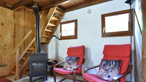 Una habitación acogedora con interior de madera, una chimenea, dos sillones rojos con cojines decorativos, una escalera de madera y una ventana con vistas.