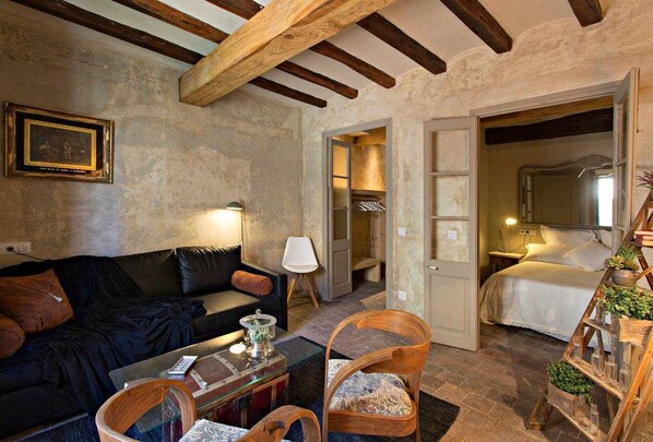 A cozy room with a dark leather sofa, a wooden chair, a glass coffee table, and a bed with a wooden ladder.