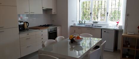 A modern kitchen with white cabinets, a gas stove, and a dining area with a glass table and chairs.