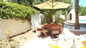 A poolside area with a table and chairs, a sun umbrella, and lounge chairs. - Beautiful Villa in front of the sea. House in first line of sea. (Santa Eulària des Riu)