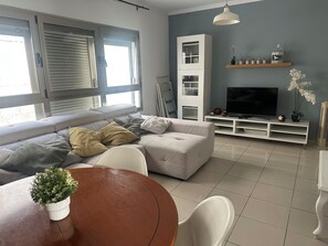 Una sala moderna con sofá, televisor y comedor con mesa y sillas.