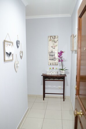 A hallway with a wooden door, a small table with decorative items, and wall-mounted artwork.