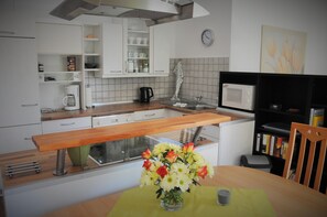 Une cuisine moderne avec des meubles blancs, un plan de travail en bois, un évier, un four à micro-ondes et un coin repas comprenant une table et des chaises.